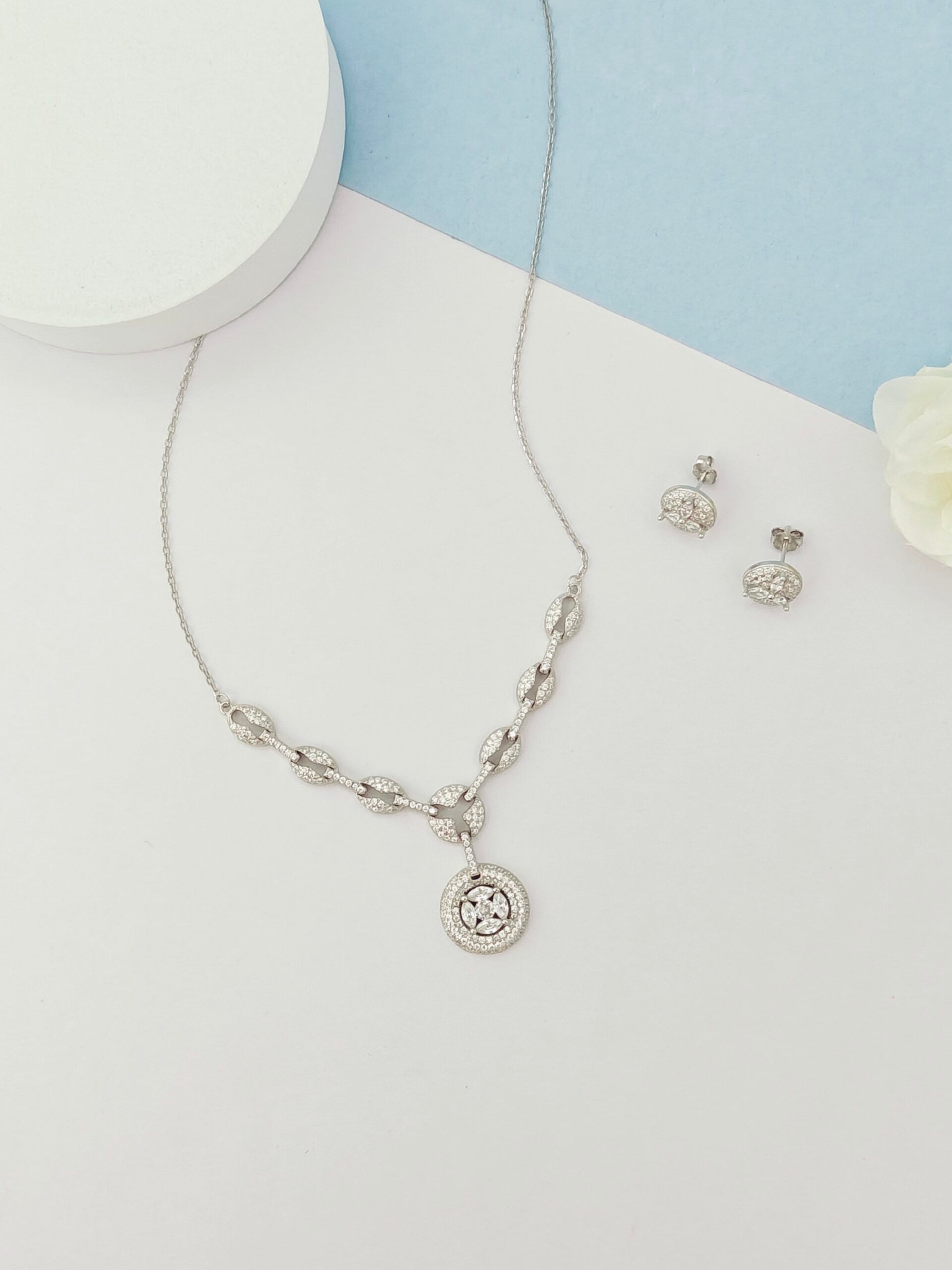 Silver necklace and earrings on a white surface with a light blue background